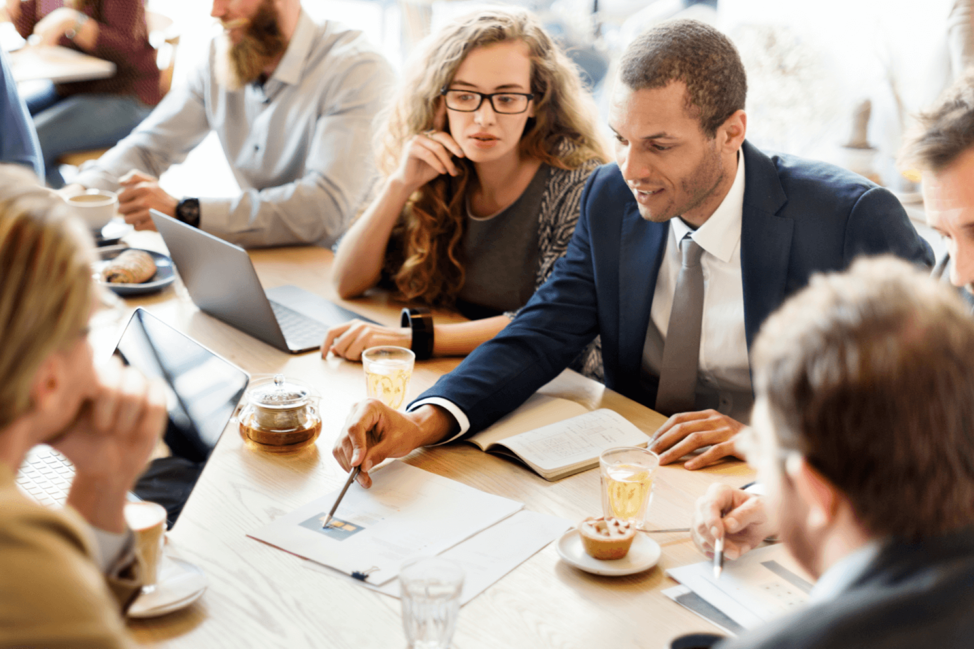 6 people sitting at a table looking at a graph with papers and laptops in front of them