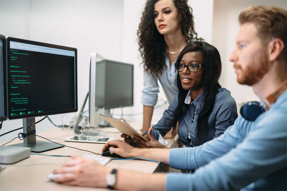 Three co-workers gatherd at a workstation looking at a monitor